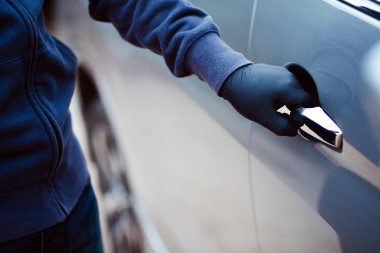 un ladrón con un guante intenta abrir la puerta de un automóvil